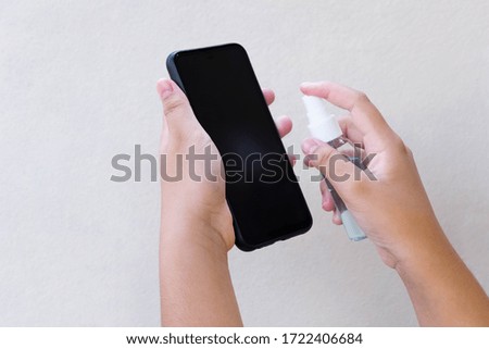 Woman's hands alcohol spray disinfectant on mobile phone to clean and protect against viruses.