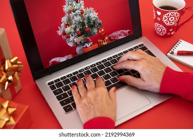 Woman's Hands Browsing On Laptop At Christmas Time - Red Background With Christmas Presents And Cup Of Tea