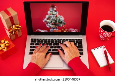 Woman's Hands Browsing On Laptop At Christmas Time - Red Background With Christmas Presents And Cup Of Tea