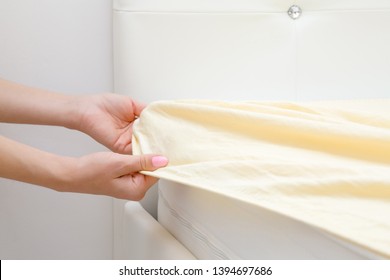 Woman's hands changing light yellow sheet on white mattress. Regular bed linen change. Closeup. Side view. - Powered by Shutterstock