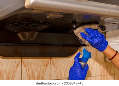 Woman's hands cleaning or servicing kitchen chimney wearing rubber gloves and using cleaning liquid..