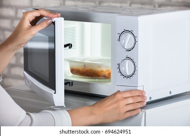 Руки женщины закрывая дверь микроволновой печи и готовая еду дома
