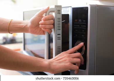 Женские руки закрывая дверь микроволновой печи и готовая еду в микроволновой печи.