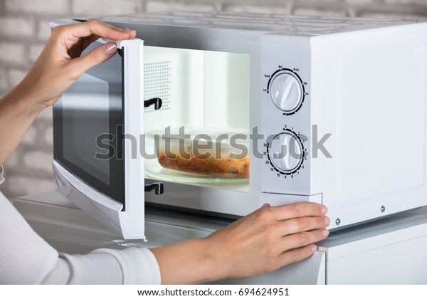 Woman's Hands Closing Microwave Oven Door And
Preparing Food At Home