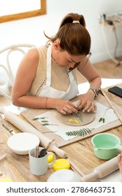 Woman's hands creating a unique ceramic piece, decorating soft clay with dried flowers and leaves