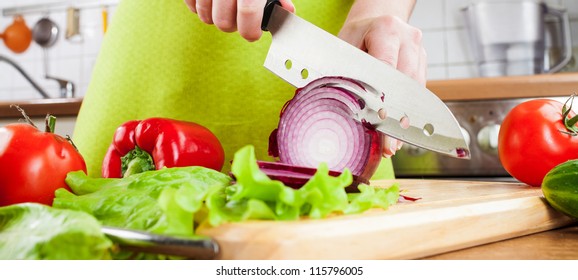 Woman's hands cutting bulb onion, behind fresh vegetables.