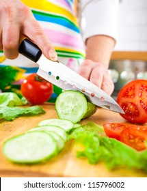 Woman's hands cutting cucumber, behind fresh vegetables.