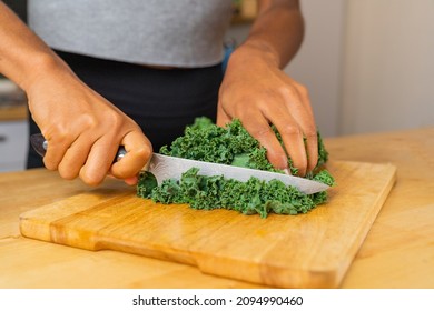 Woman's hands cutting kale leaves with a large kitchen knife on a wooden cutting board  Concept of super food, healthy and vegetarian food  - Powered by Shutterstock