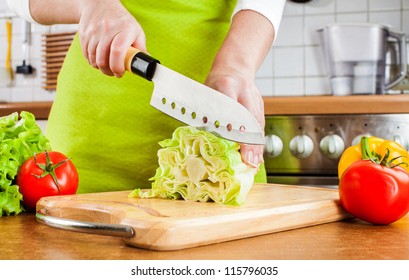 Woman's hands cutting lettuce, behind fresh vegetables.