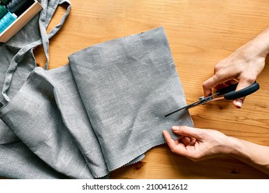 Woman's hands cutting out a pattern paper in linen fabric. Seamstress sewing on sewing machine in small studio. Fashion atelier, tailoring, handmade clothes concept. Slow Fashion Conscious consumption