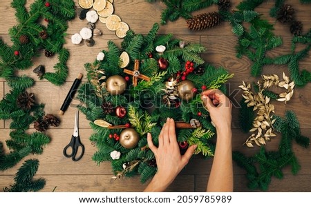 Woman's hands decorating a Christmas wreath. New Year holiday decoration, Christmas tree wreath decoration with female's hands DIY.