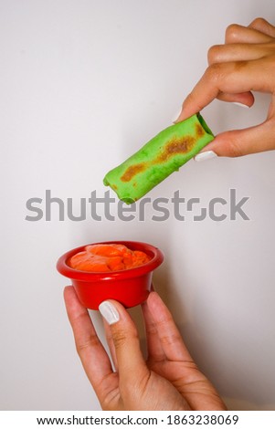 Woman's hands dipping a shawarma roll on sauce with plain background