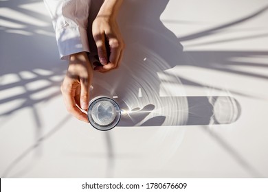 Woman's Hands And A Glass Of Clean Water On The White Table In Natural Sunlight With Plant Shadows. Minimalist Lifestyle Concept