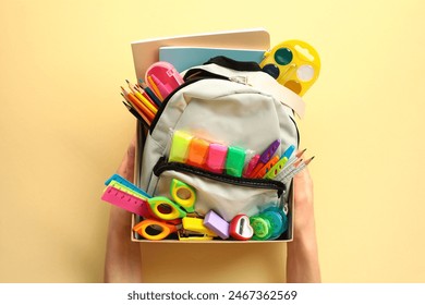 The woman's hands hold a donation box with a backpack containing various school supplies. Donation concept. - Powered by Shutterstock