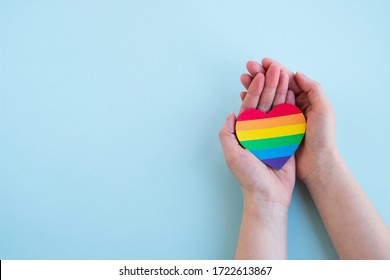 Die Hände der Frauen halten Herz in den Farben des Regenbogens auf hellblauem Hintergrund. LGBT-Konzept, Pride Monat. Draufsicht, Kopienraum