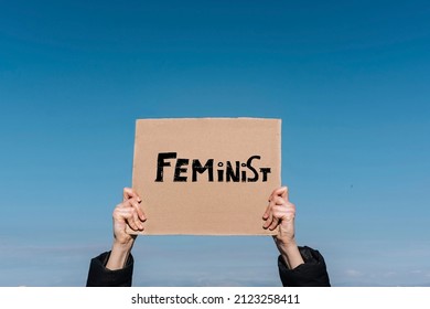 Woman's Hands Hold A Sign With The Word FEMINIST With The Sky In The Background. Feminist Concept. Copy Space.