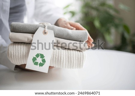 Woman's hands hold a stack of clean neat knitted clothes with a recycle  label. Recycle Icon show on Tag. Recycling Products Concept.