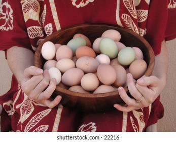 A woman's hands hold a wooden bowl full of different naturally colored eggs.