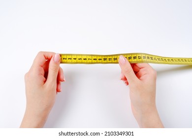 The woman's hands hold a yellow measuring tape on a white background.Measurement of length and circumference.The concept of weight loss, diets.Workshop for sewing and repairing clothes.Top view. - Powered by Shutterstock