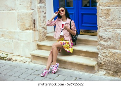 Woman's Hands Holding Beige Trendy Clutch Bag In Front Of The Old City Street Over Wall In Summer Time Outside In The Streets. Fashion Accessories. Street Style Summer Spring Photo,floral Sneakers