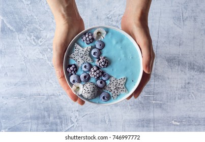 Manos de mujer sosteniendo el yogur azul Smoothie Bowl hecho con polvo de espirulina azul, bayas congeladas y fruta del dragón