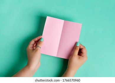 Woman's hands are holding empty mock-up brochure for writing letter above pastel turquoise background