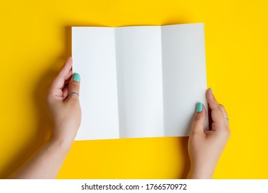 Woman's hands are holding empty trifold mock  up brochure for writing letter above yellow background