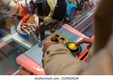 Woman's hands holding a joystick of a hook machine to catch toys in an arcade. Close-up image of a girl's hands pressing a button and moving a selector lever of an arcade machine.