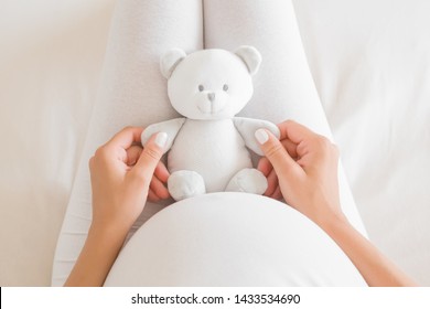 Woman's hands holding little smiling white teddy bear on lap for future baby. Homely atmosphere. Emotional loving moment in pregnancy time - 35 weeks. Baby expectation. - Powered by Shutterstock