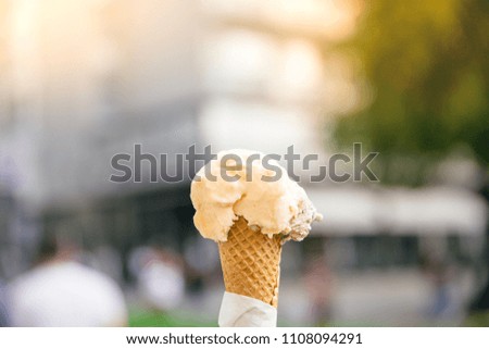 Woman's hands holding melting ice cream waffle cone in hands on summer blur background.