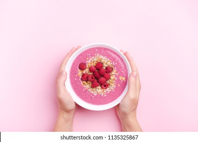 Woman's hands holding raspberries smoothie bowl on pink background. Top view, copy space. - Shutterstock ID 1135325867