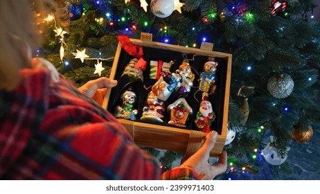 woman's hands holding wooden box with vintage Christmas ornaments with christmas tree on background. 