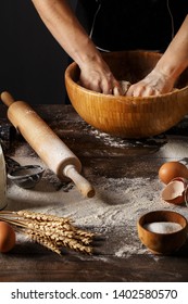 Woman's hands kneading dough in wooden bowl on table with spelt flour, raw eggs, rolling pin and wheat spikes. Step by step recipe of cooking dough, bakery products or pastry