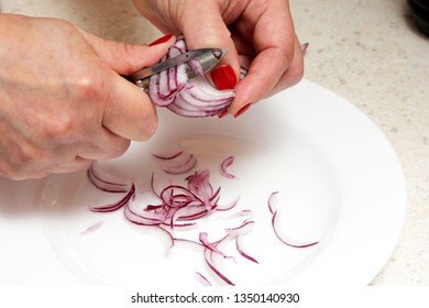 Woman's hands with a knife cut onion on a white plate