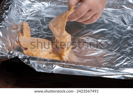 woman's hands lay out marinated chicken wings on foil for baking. Horizontal photo.