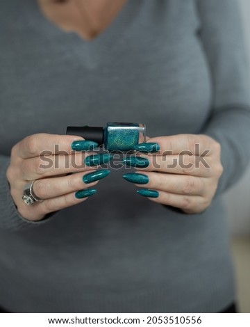 Woman's hands with long nails and turquoise blue green manicure with bottles of nail polish	