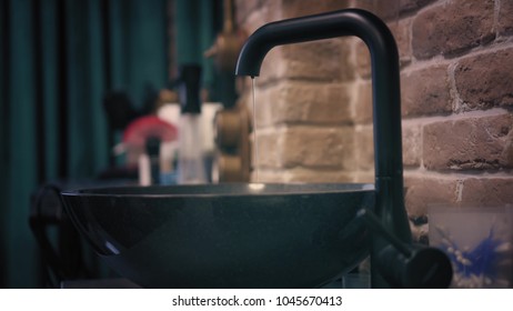 Woman's hands with lovely pink manicure softly turn on black water tap. Satisfying closeup view on water flows