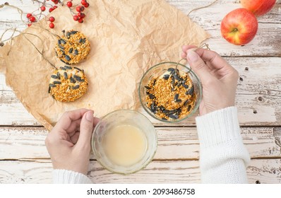 The Woman's Hands Make Food For Wild Birds From Apple, Bacon And Seeds. Winter Bird Feeder On A White Wooden Background. View From Above.