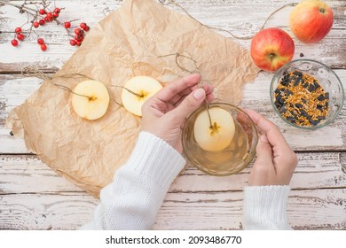 The Woman's Hands Make Food For Wild Birds From Apple, Bacon And Seeds. Winter Bird Feeder On A White Wooden Background. View From Above.