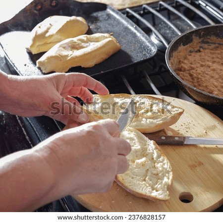 Woman's hands making MOLLETES as part of a classic Mexican breakfast with bread, butter, beans, cheese, salsa and avocado.