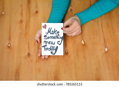 Woman's hands and a note with make something new today text on rustic wooden table
