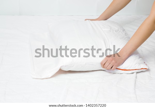 Woman\'s hands on\
mattress surface changing white cotton cover on pillow. Regular bed\
linen change. Closeup. 