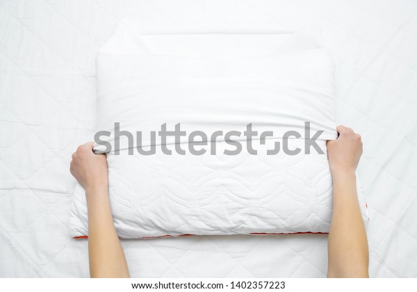 Woman\'s hands on mattress surface changing white\
cotton cover on pillow. Regular bed linen change. Closeup. Point of\
view shot.