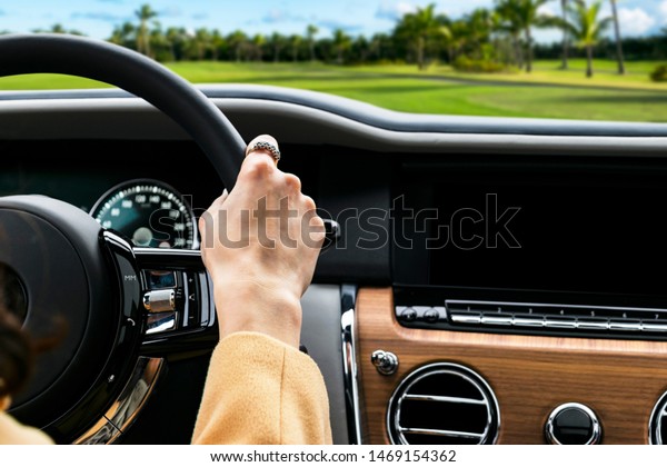 Woman\'s hands on the steering\
wheel driving modern luxury car. Concept woman driving. Hands\
holding steering wheel while driving. Car inside. Car\
detailing.