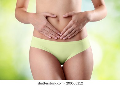 Woman's hands on stomach on green background heart symbol
