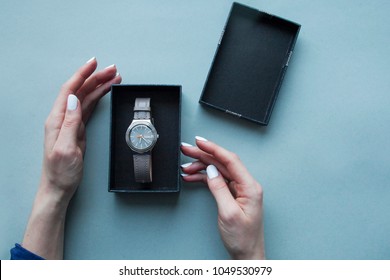 Womans hands opens black gift box with grey watchs. Flat lay. Top view. Space for text. Grey background. Luxury gift
