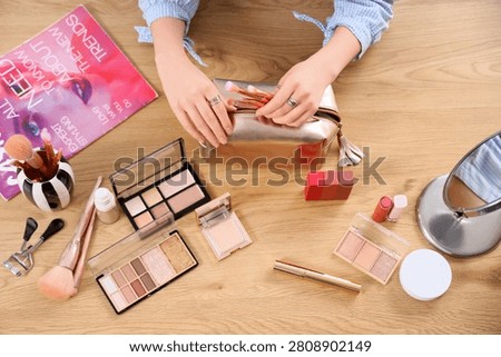 Womans hands organizing makeup brushes into a cosmetic bag on a wooden table with Various beauty products