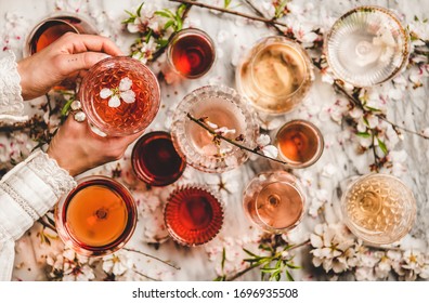 Womans hands over dofferent shades of rose wine in glasses and spring blossom flowers over white background, top view. Wine shop, bar, wine tasting, wine list concept