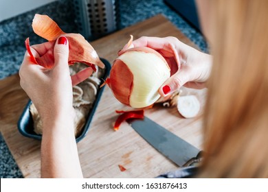 A woman's hands peeling an onion with a knife in a kitchen. A tray of mushrooms is seen on a wooden board. Healthy vegetarian or vegan food