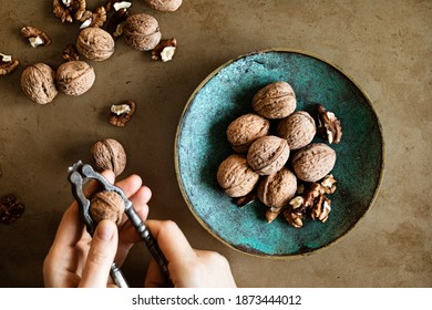 Woman's Hands Peeling Walnuts With A Nutcracker On A Table, Overhead View